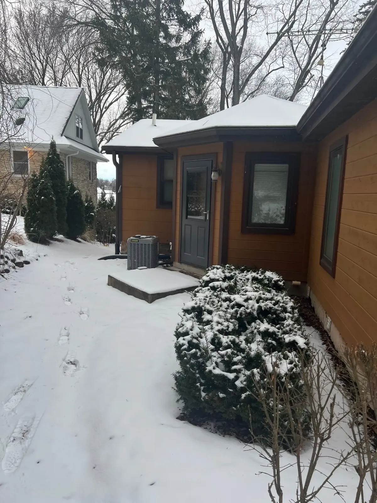 Snow-covered side entry and outdoor air conditioning unit checked during a winter home watch visit