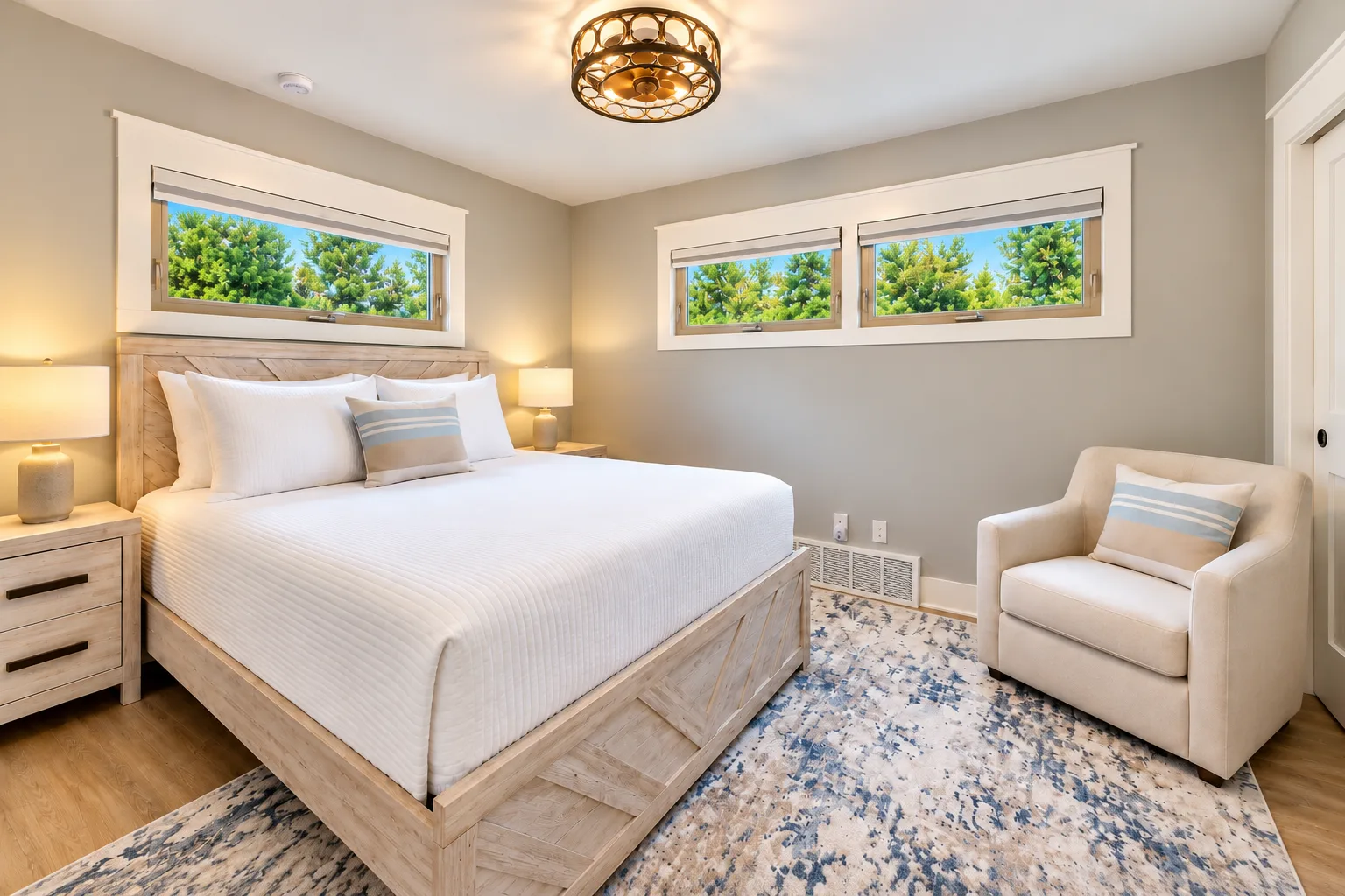 Bright bedroom with a light wood bed frame, white bedding, and windows looking out on evergreen trees