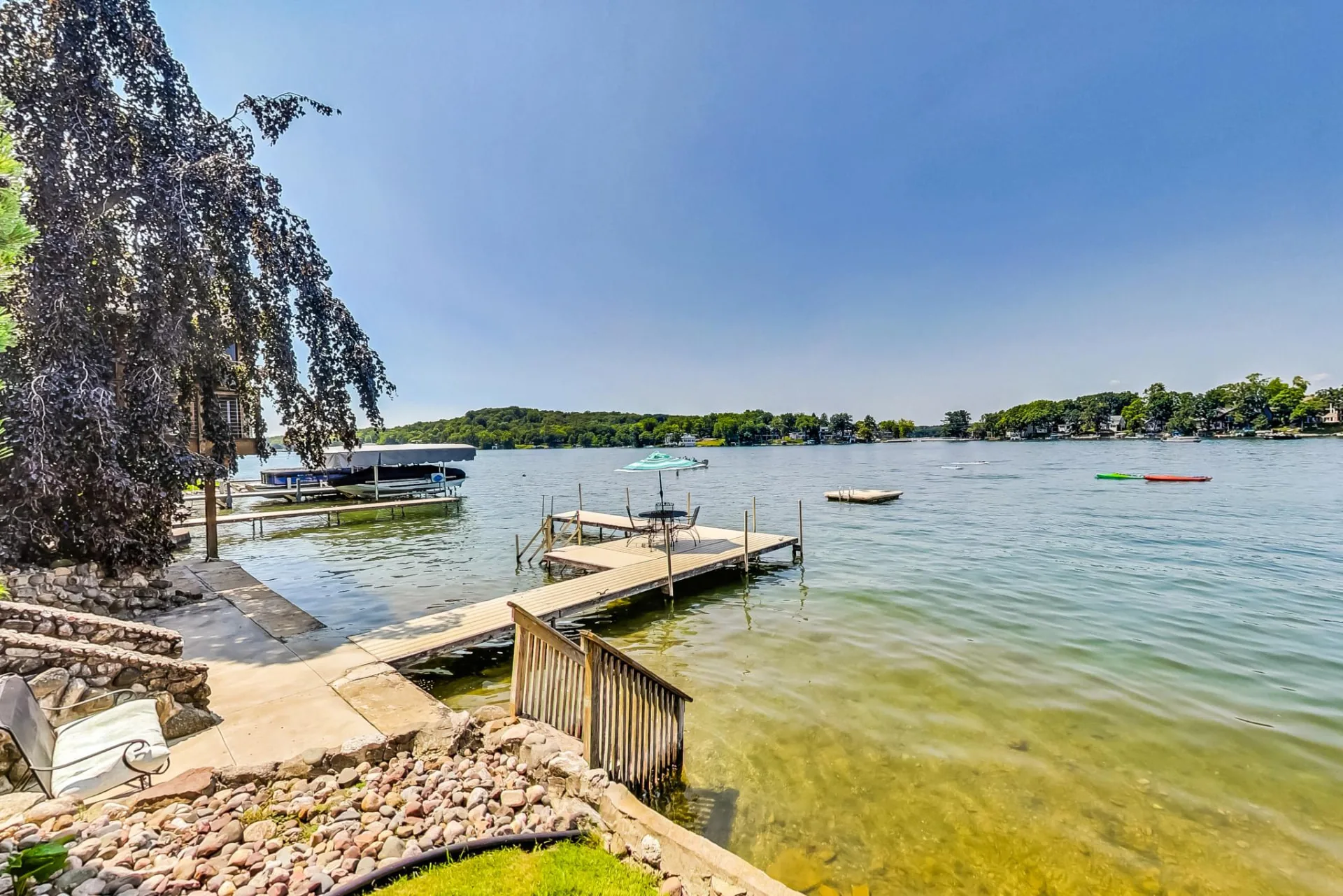 Dock with a patio table and umbrella on Lauderdale Lakes, kayaks on the water and a tree-lined shore behind